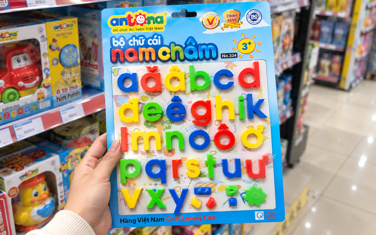 Bàn tay cầm bộ chữ cái nam châm Antona nhiều màu sắc tại cửa hàng đồ chơi trẻ em, sản phẩm giáo dục giúp bé từ 3 tuổi làm quen chữ cái tiếng Việt.