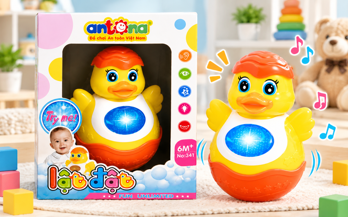 Đồ chơi lật đật vịt Antona màu vàng cam, có đèn phát sáng và âm thanh, được trưng bày cùng hộp sản phẩm, phù hợp cho bé từ 6 tháng tuổi theo nhãn sản phẩm.